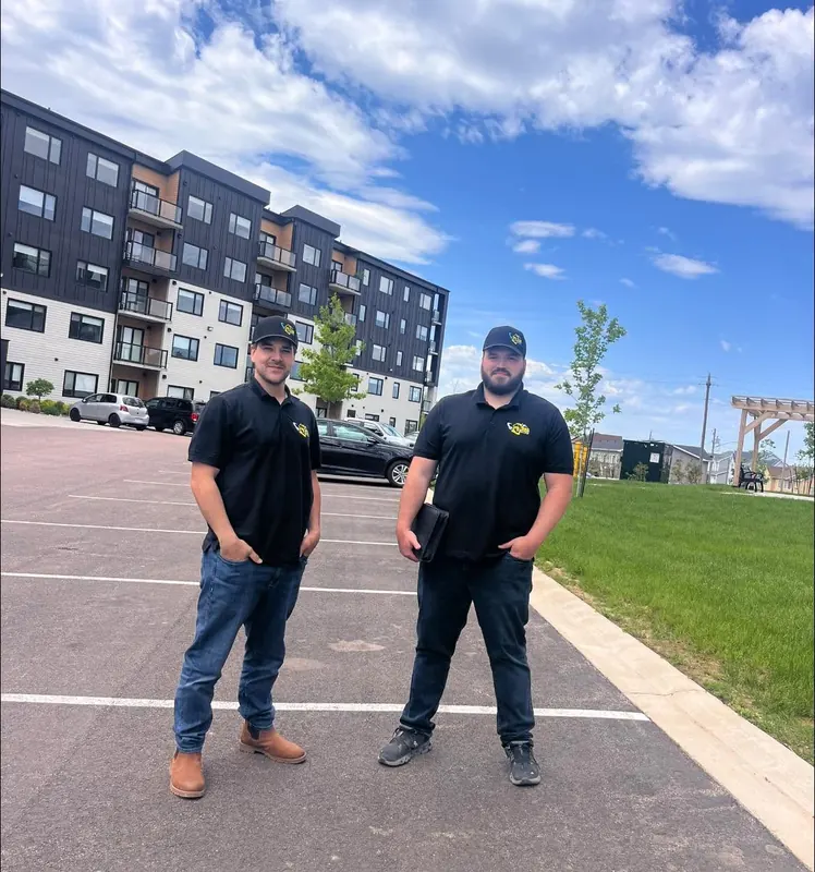 Two RJS team members standing in front of a multi-unit apartment development