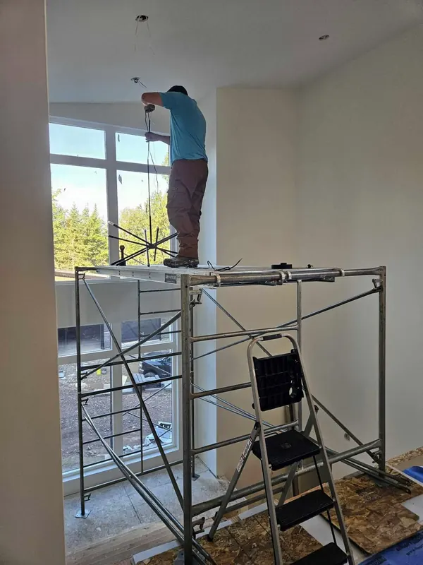 Electrician on scaffolding installing a chandelier in a tall great room