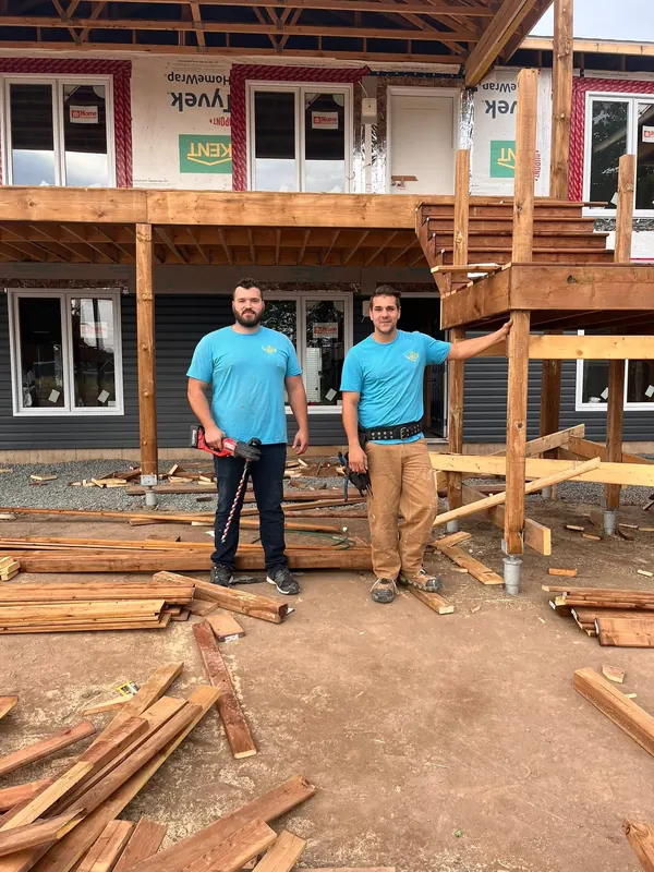 Rejean and Shawn of RJS Electric in cyan RJS t-shirts in front of a house under construction